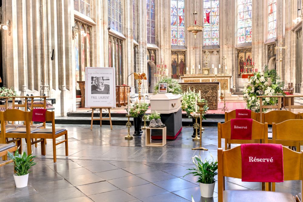 Cérémonie de funérailles dans l'église du Salon à Bruxelles. Des fleurs de lunes en pot décorent l'allée.